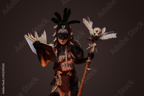 Studio shot of furious voodoo witch holding staff with skull and book of dead.