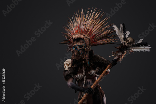 Shot of scary aztec necromancer holding staff with skull against grey background. photo