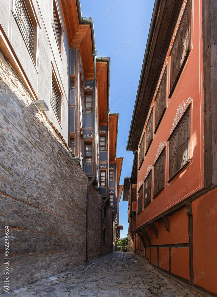 Narrow cobbled street unites 2 different architectural eras: ancient Roman Acropolis stonework and BULGARIAN REVIVAL MUSEUM EXHIBITION Renaissance building of 19th century, vertical, Plovdiv, Bulgaria