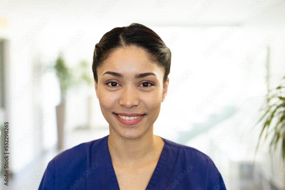 Portrait of smiling biracial female healthcare worker in hospital corridor, with copy space Portrait of smiling biracial female healthcare worker in hospital corridor, with copy space