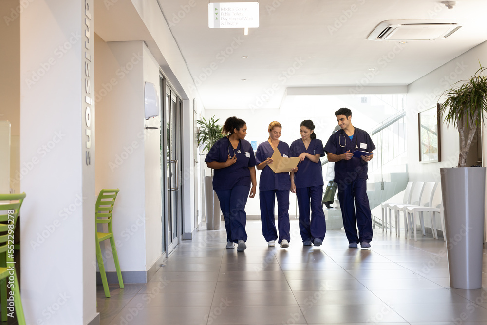 Fototapeta premium Diverse group of happy male and female doctors talking walking in hospital corridor, with copy space