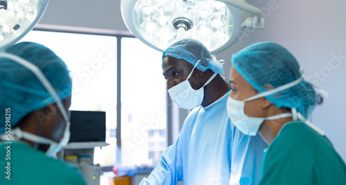 Three diverse male and female surgeons working in operating theatre during operation