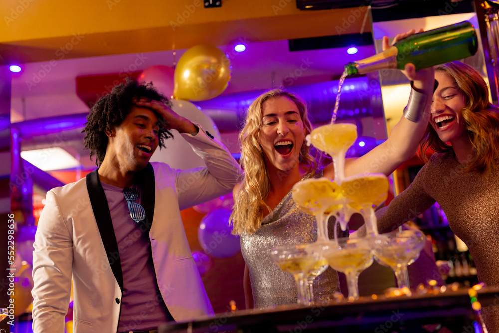 Happy caucasian woman pouring a champagne fountain into glasses with diverse friends at a nightclub