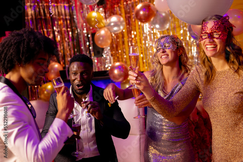 Four happy, diverse friends laughing and drinking glasses of champagne at a party in a nightclub