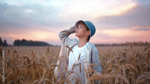 teenager boy in a golden wheat field looks at the beautiful colorful sky in the weather after rain at sunset, steadicam shot