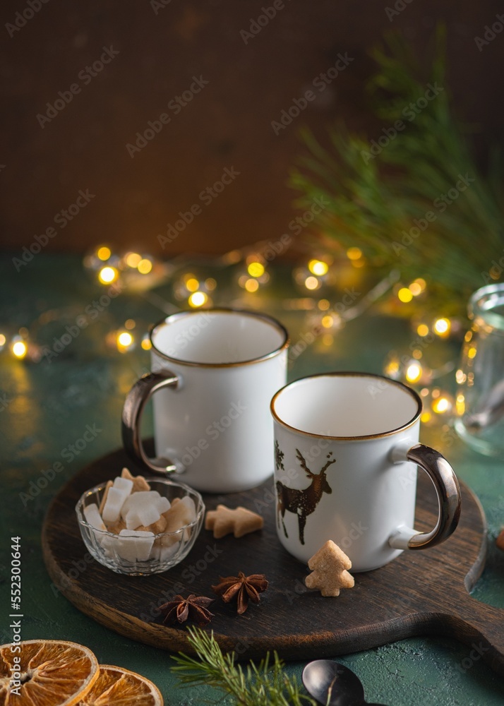 Fototapeta premium Two empty white mugs on a wooden board on a green concrete background in a Christmas composition. Prepared serving for hot drinks.