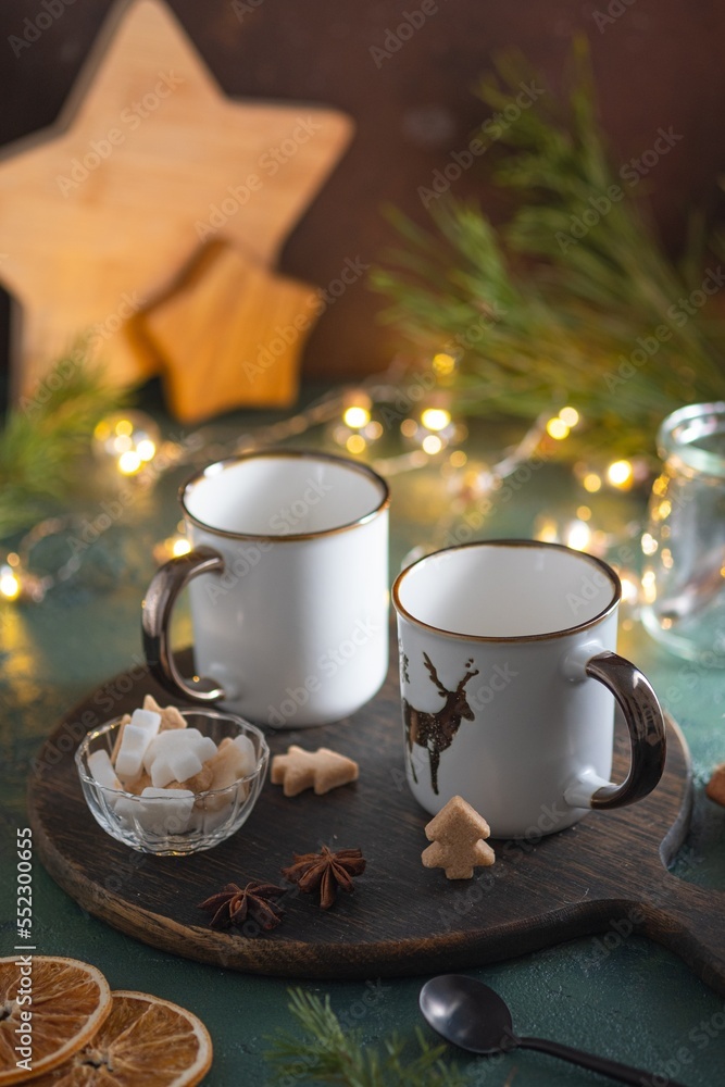 Two empty white mugs on a wooden board on a green concrete background in a Christmas composition. Prepared serving for hot drinks. Two empty white mugs on a wooden board on a green concrete background in a Christmas composition. Prepared serving for hot drinks.