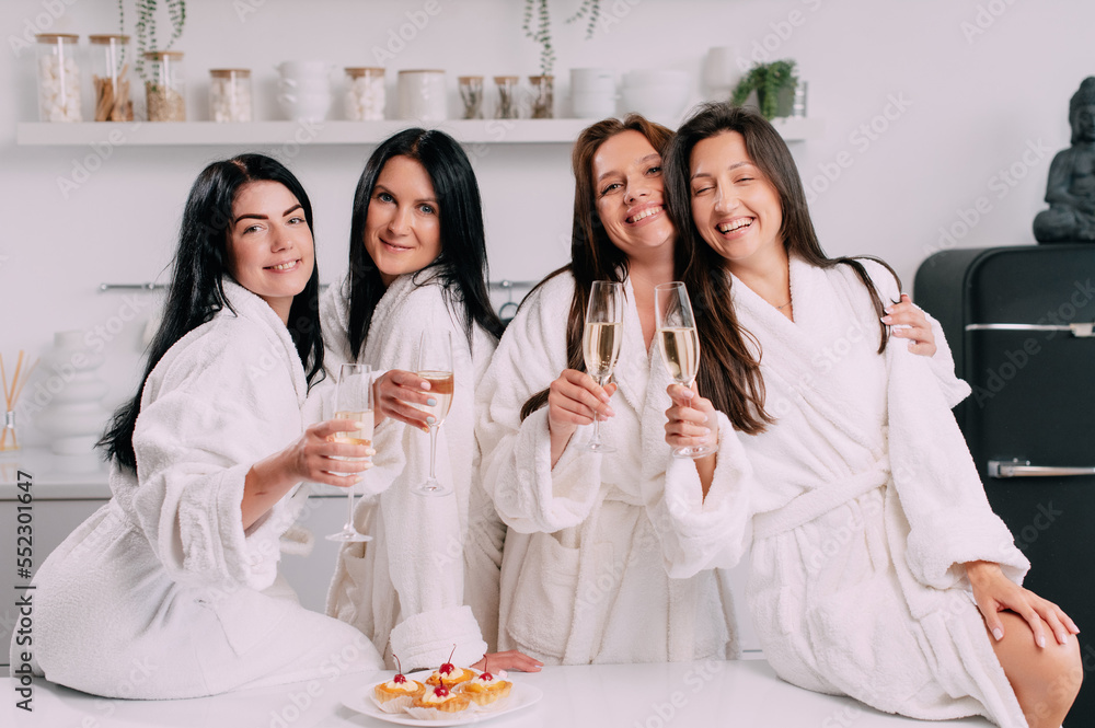 A group of women spend leisure time. Young attractive females in bathrobes drink champagne and chat merrily at home. A group of women spend leisure time. Young attractive females in bathrobes drink champagne and chat merrily at home.