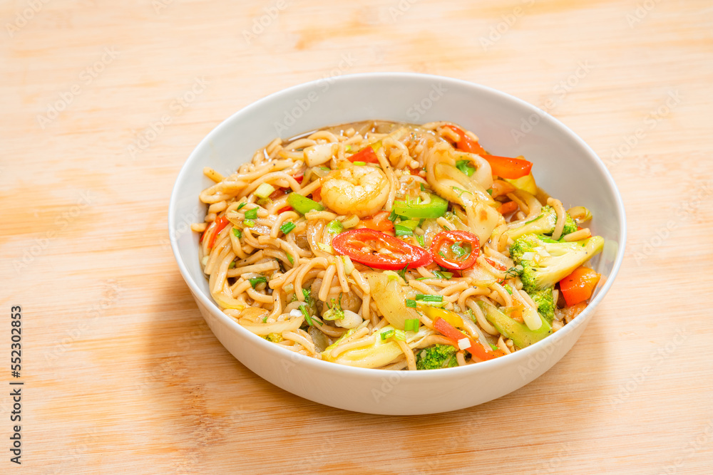 Golden coloured spicy sea food noodles with shrimp, broccoli, chilli pepper in a plate on wooden table