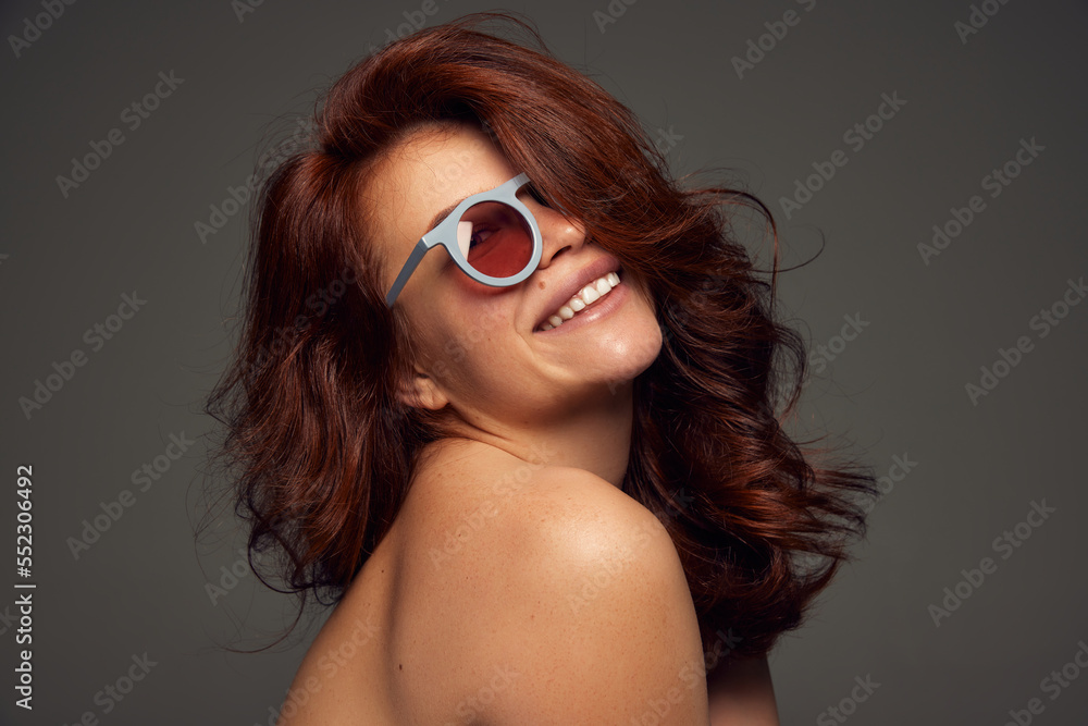Portrait of young beautiful red-haired woman with perfect wavy hair smiling, posing isolated on dark grey background. Portrait of young beautiful red-haired woman with perfect wavy hair smiling, posing isolated on dark grey background.
