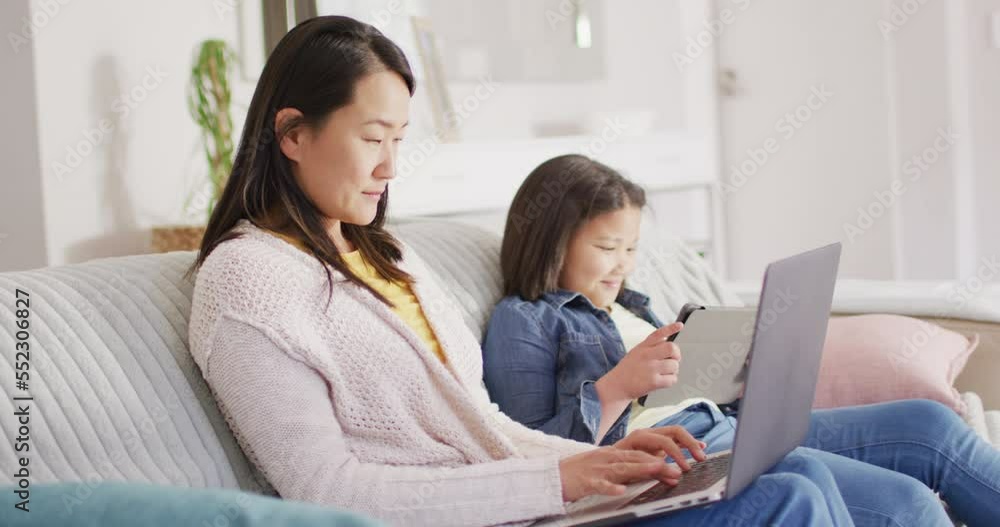 Video of happy biracial mother and daughter sitting on sofa with laptop and tablet Video of happy biracial mother and daughter sitting on sofa with laptop and tablet