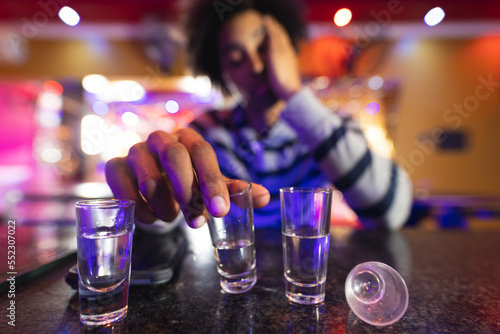 Drunk african american man sitting at the bar with shot glasses, selective focus