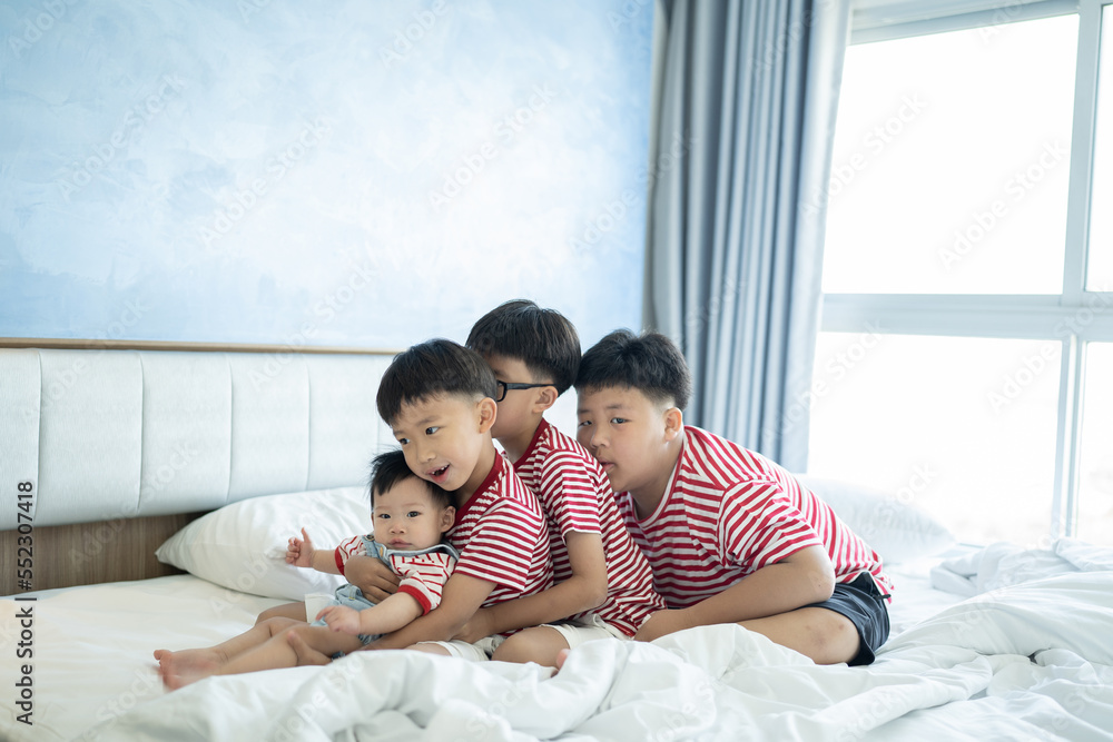Fototapeta premium Brothers and baby sister is playing on the white bed in the bedroom.The selective focus and space for copy and text.