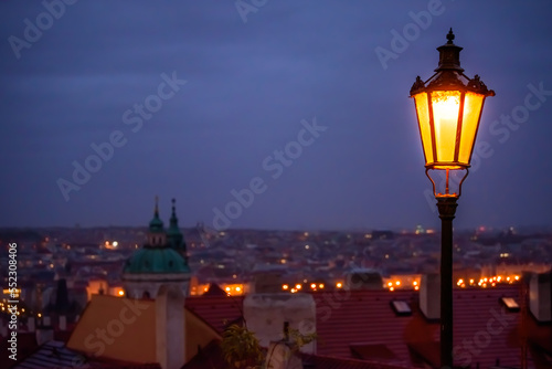 Photography A shining lamp above the Prague cityscape in the evening.
