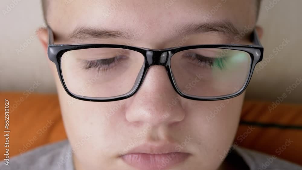 Close-up Part of the Face of a Child with Glasses Watching on Screen TV in Room. Boy with long eyelashes. Reflection glare light in glasses. Poor eyesight. Macro. Internet, reading, working online. Close-up Part of the Face of a Child with Glasses Watching on Screen TV in Room. Boy with long eyelashes. Reflection glare light in glasses. Poor eyesight. Macro. Internet, reading, working online.