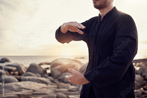 Beach, peace and tai chi, man in nature for balance and peace for mental wellness or control of body and mind. Spiritual health, fitness and meditation, energy and self care on rocks at sea in sunset photo