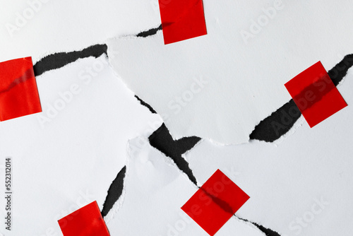 Ripped up pieces of white paper stuck together with red tape on black background