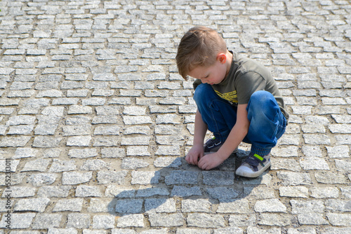 Boy sitting on the cracked earth and shows tongue. Boy five years old sits on a city pavement. High quality photo © Luci