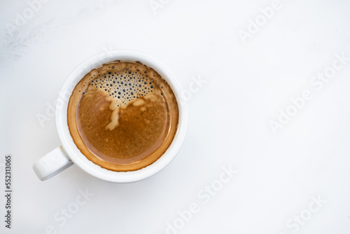 White cup of cappuccino coffee on white textured marble background. Close-up shot, top view. copyspace