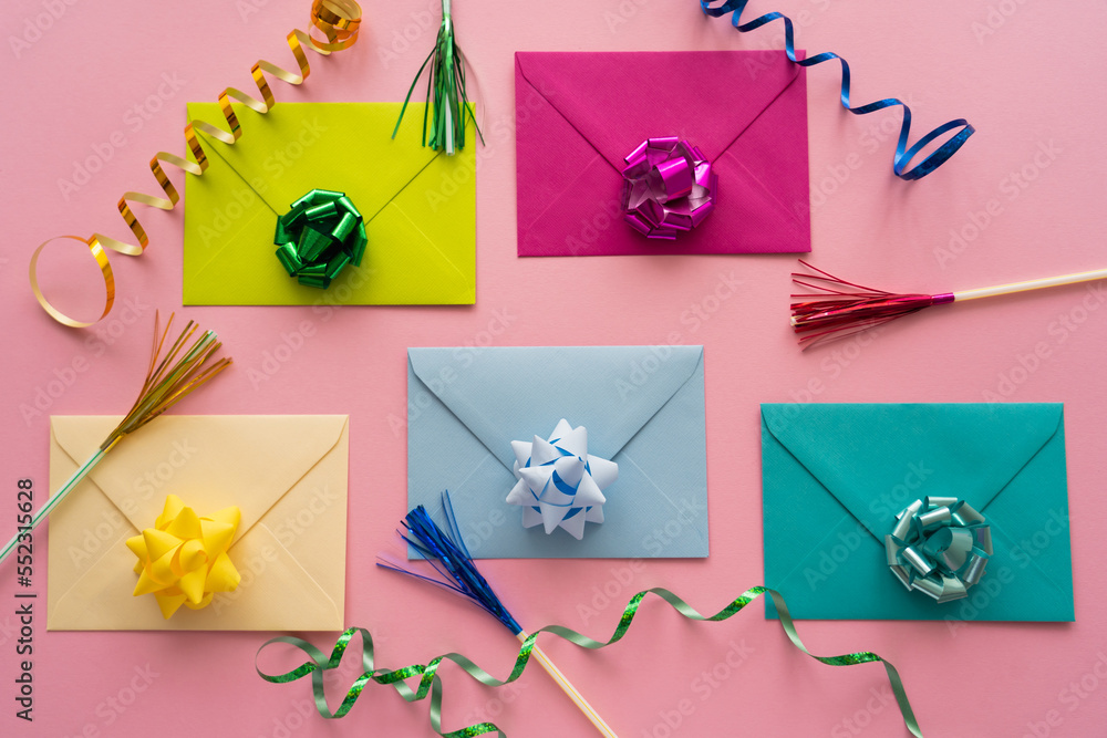 Top view of colorful gift bows on envelopes near serpentine on pink background.