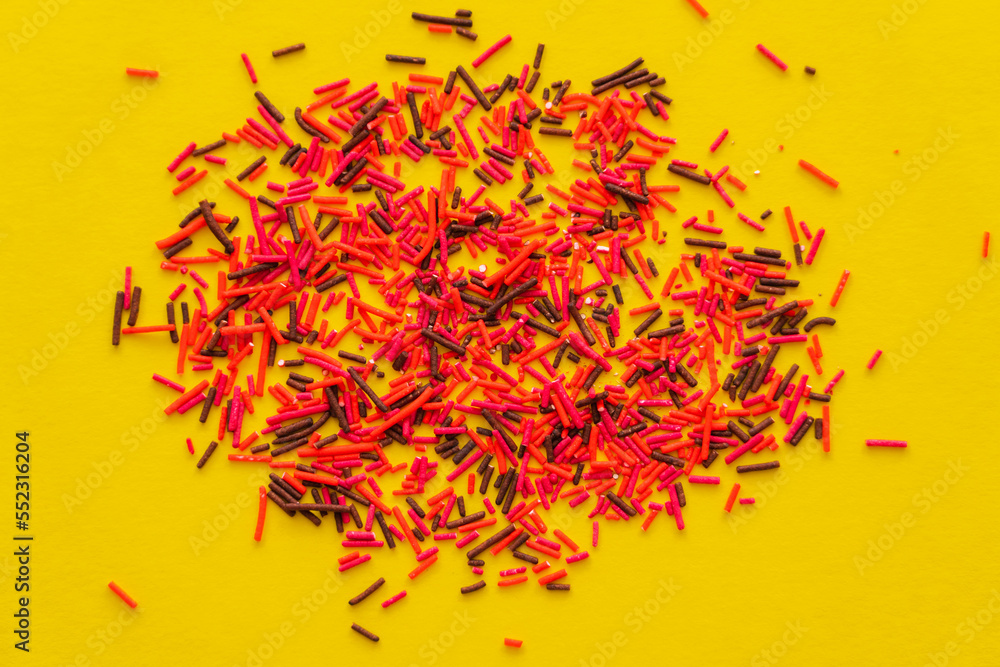 Naklejka premium Top view of colorful sprinkles on yellow background.