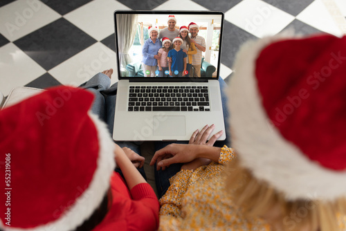 Caucasian mother and daughter in santa hats on christmas laptop video call with caucasian family