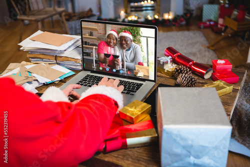 Santa claus with christmas presents having video call with happy african american couple