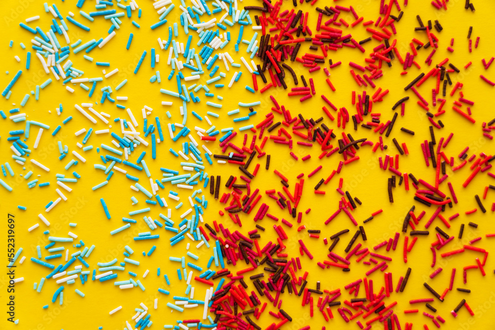 Top view of colorful sweet sprinkles on yellow background.