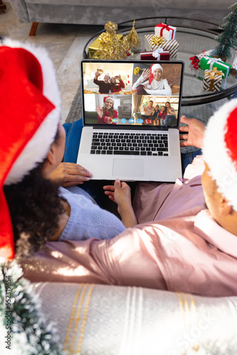 Biracial couple with santa hats having video call with happy caucasian friends