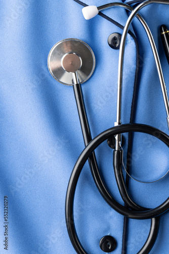 Vertical composition of stethoscope and pen on blue nurse's uniform shirt, copy space