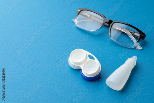Composition of glasses with contact lenses case and eye drops and on blue background with copy space