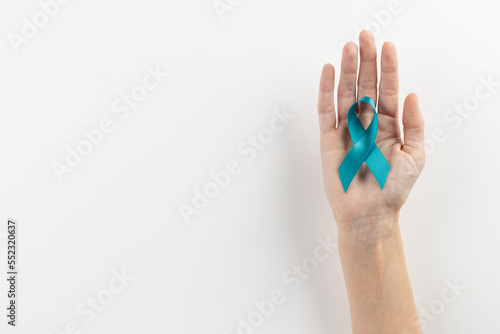 Composition of hand holding blue ovarian cancer awareness ribbon on white background with copy space