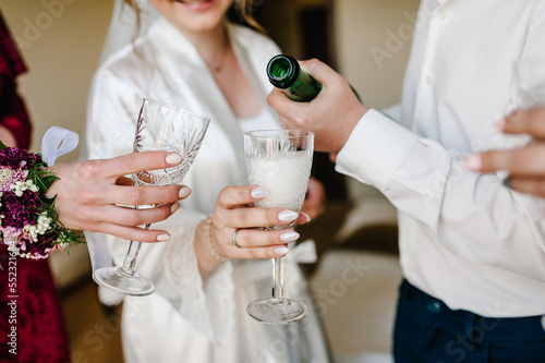 Bridal morning with bridesmaids drinking champagne. Bride wearing silk pajamas. Girls and man at the party with champagne glasses. Bridesmaid with bride and groom drink champagne before the wedding.