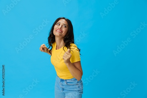 Woman in yellow t-shirt on blue background posing gestures emotions and signals with smile, hands up happiness copy space