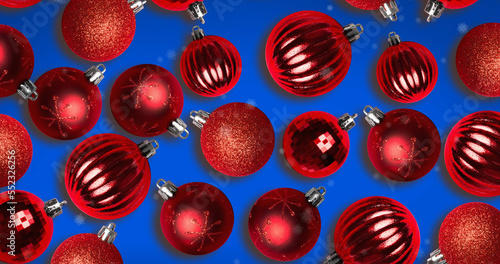 Image of snow falling over christmas bauble decorations on blue background