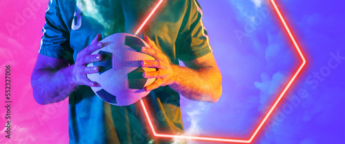 Midsection of biracial male player holding ball with illuminated hexagon shape on colored background