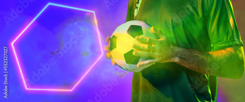 Midsection of caucasian male player holding ball by illuminated hexagon on blue background