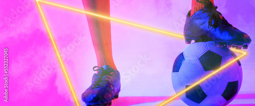 Low section of male player with leg on ball by illuminated triangle over smoky pink background