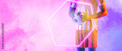 Midsection of african american male player with ball and illuminated hexagon over smoky background