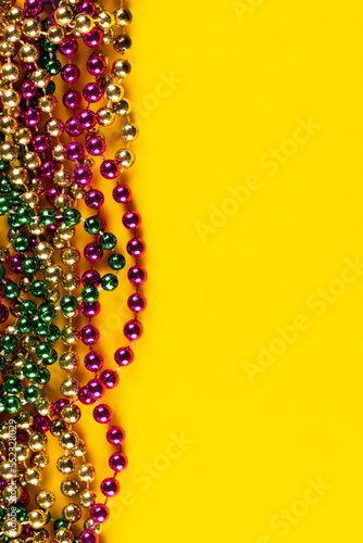 Composition of colourful mardi gras beads on yellow background with copy space