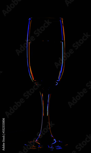 One glass of champagne in the background lighting on a black table. Silhouette of a champagne glass on a black background in a colored background.