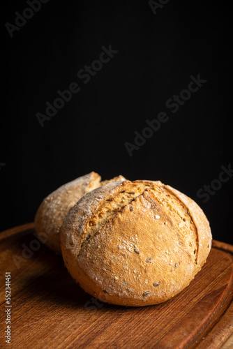 closeup of two quinoa buns on wooden board, black background, vertical, with copy space