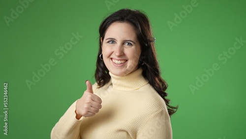 Smiling happy satisfied young woman 20s turn around to camera showing thumbs up like gesture isolated on green screen background studio portrait. People lifestyle concept