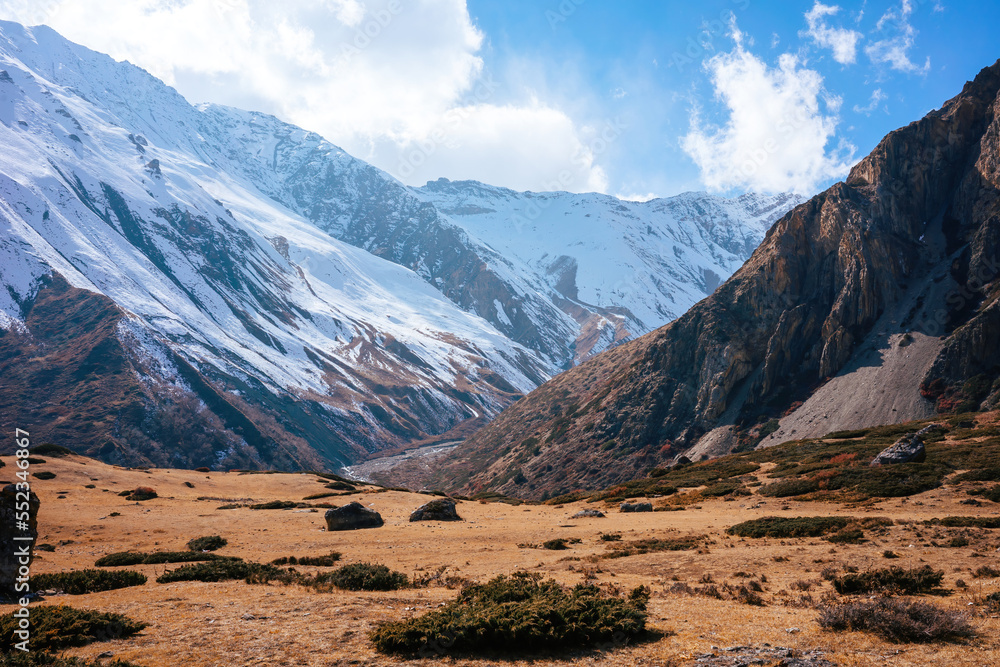 Brown rocky mountain with snow on the peak against a beige barren landscape at day and blue sky. Annapurna mountain range in the Himalayas of Nepal