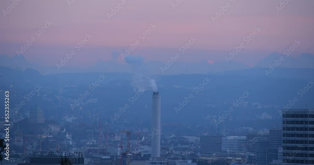 Tall smokestack or industrial chimney emitting white smoke or steam. Zurich city Switzerland, evening after sunset, close up telephoto shot. Visible Alps in the background, no people Tall smokestack or industrial chimney emitting white smoke or steam. Zurich city Switzerland, evening after sunset, close up telephoto shot. Visible Alps in the background, no people