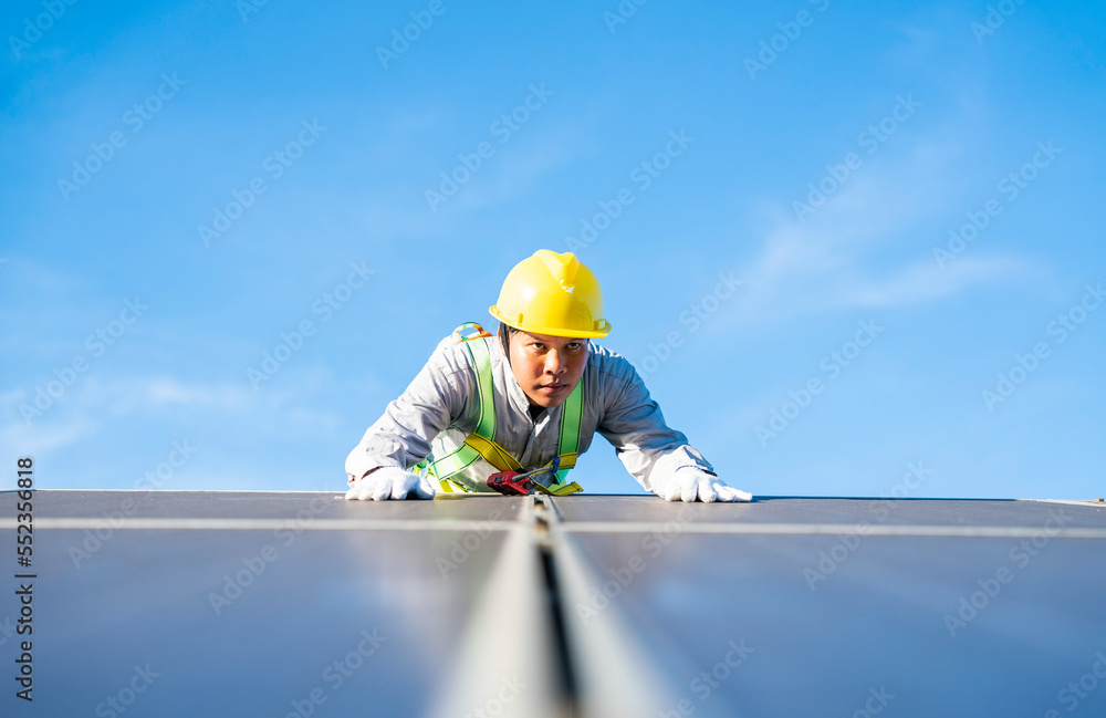 Fototapeta premium MaleAsia technician wearing protective clothing for safety climbs to install solar panel at solar farm using sunlight to produce solar electricity.Renewable Energy and Electricity Concept