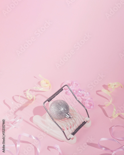 Sparkly silver Christmas ornament in egg cutter. Soft pink background with ribbons all over. New Year's concept design idea. Abstract holidays moments in December