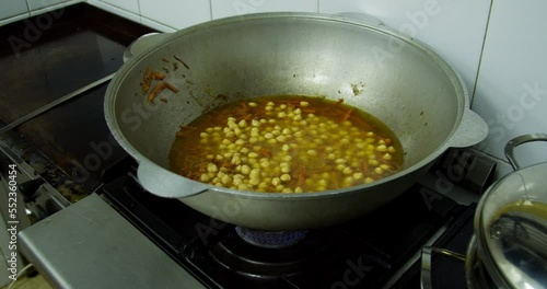 The cook pours chickpeas into a cauldron with pilaf in the kitchen