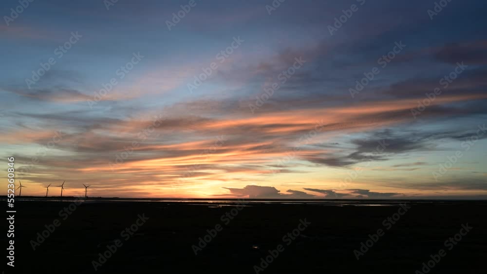 Sunset at the seaside, the windmill generating electricity turns in the wind. Qingshui District, Gaomei Wetland, Taichung City, Taiwan