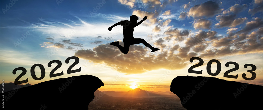 Φωτογραφία A young man jump between 2022 and 2023 years over the sun and through on the gap of hill silhouette evening colorful sky